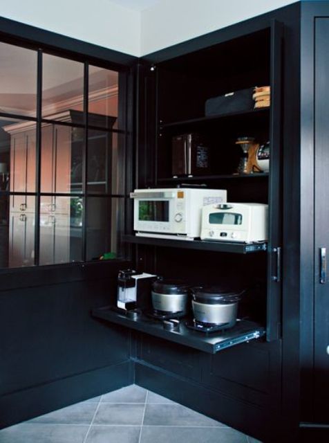 un grande armadio nero che contiene tutti gli elettrodomestici su ripiani a scomparsa aiuta a tenere in ordine la cucina e renderla più fresca