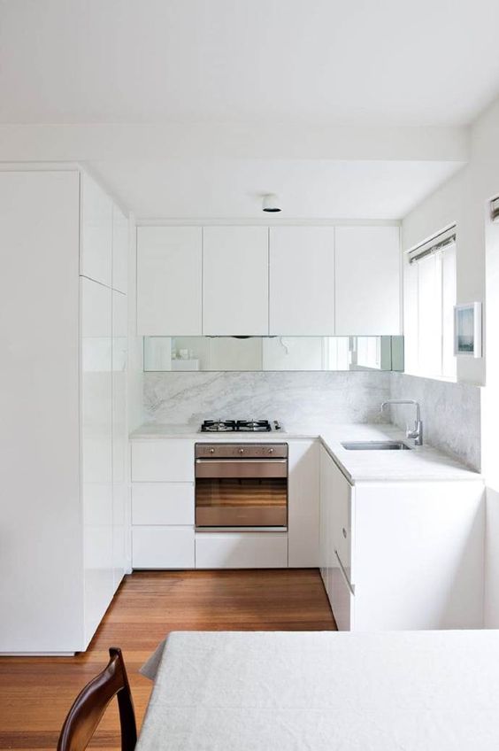 una piccola cucina minimalista con alzatina bianca e ripiani, un tocco di specchio e uno spazio per mangiare
