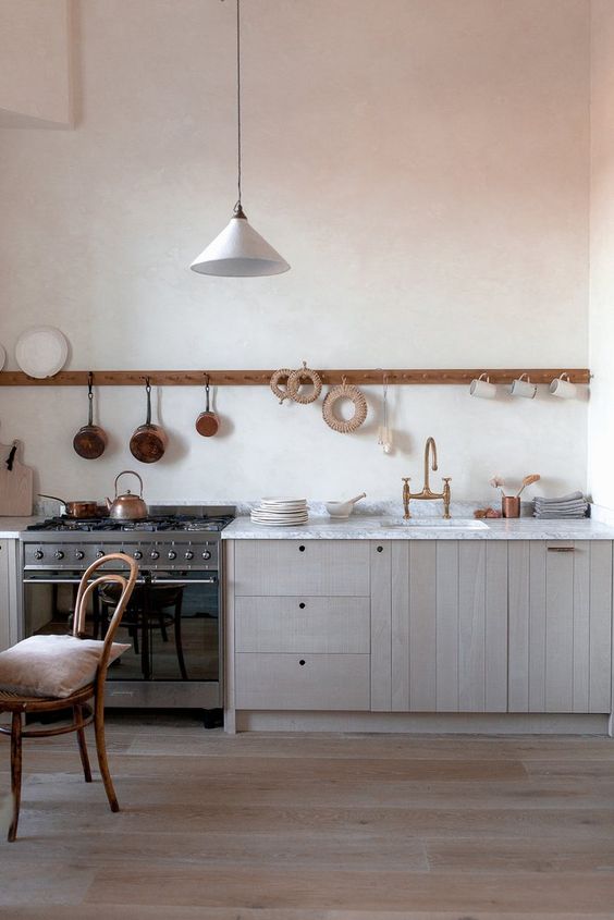 un'elegante cucina lineare in legno biondo con un piano di lavoro in pietra bianca e un supporto lungo con tazze e padelle