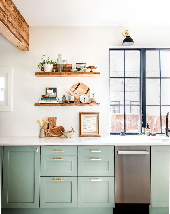 un'elegante cucina verde in stile rustico, un piano di lavoro in pietra bianca e mensole a giorno, travi in ​​legno e una finestra con cornice nera