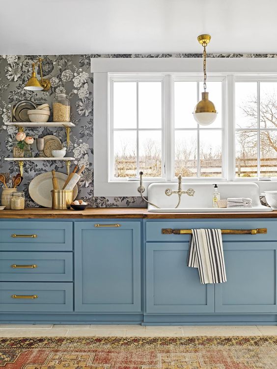 una bella cucina blu a una parete con carta da parati floreale, ripiani in macellaio e graziose lampade a sospensione vintage