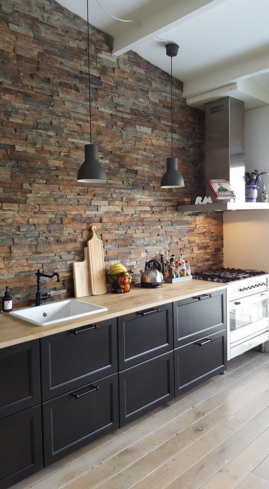 un'accogliente cucina nera lineare con ripiani in macellaio e una parete in finta pietra più lampade a sospensione è chic