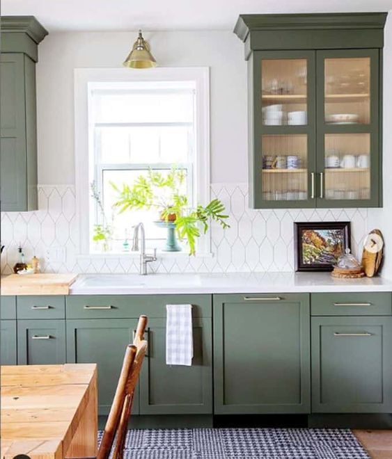 una cucina verde lineare con un grazioso alzatina in piastrelle bianche, un piano di lavoro bianco e tocchi in ottone più un tappeto stampato