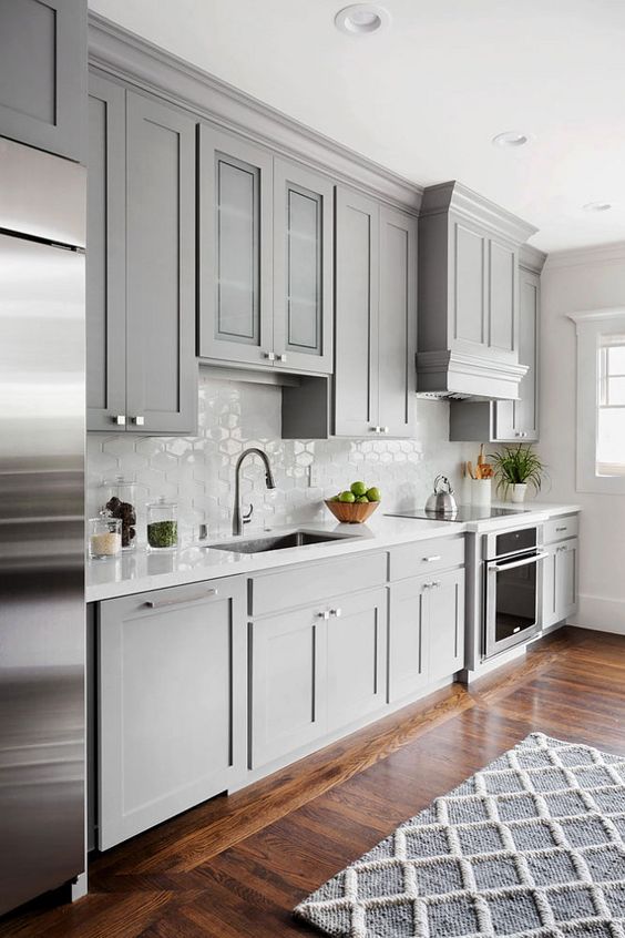 una cucina grigio chiaro con un fresco alzatina in piastrelle esagonali ed elettrodomestici in acciaio inossidabile è un'idea chic e carina
