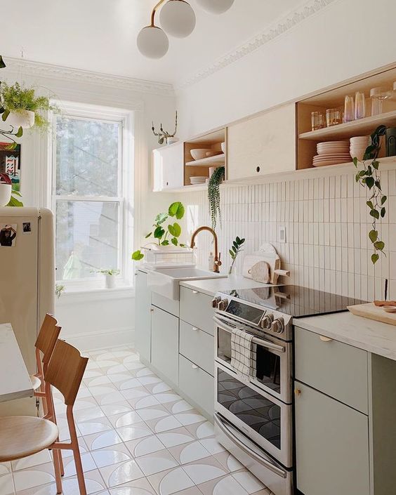 un'elegante cucina moderna di metà secolo con mobili in legno verde oliva e biondo, con alzatina in piastrelle sottili e ripiani bianchi