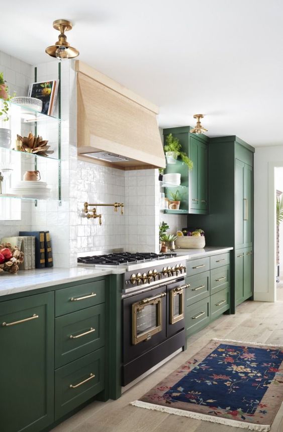 un'elegante cucina verde con cappa in legno biondo e un fornello vintage più lampade in ottone e ripiani bianchi