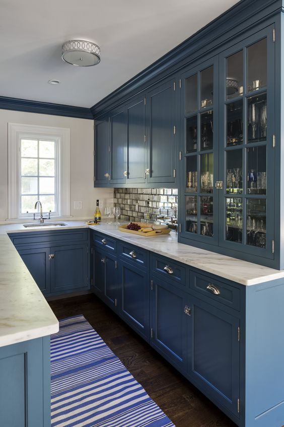 una cucina a forma di U blu con ripiani in pietra bianca e un backsplash di piastrelle a specchio è uno spazio molto elegante