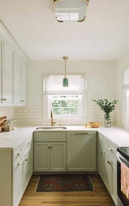 un'accogliente cucina da fattoria verde chiaro con ripiani in pietra bianca e alzatina in piastrelle bianche più una lampada vintage