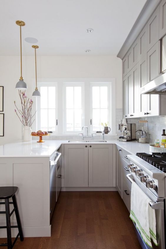 un'accogliente cucina grigia a forma di U con ripiani in pietra bianca, un backsplash in piastrelle di marmo bianco e lampade eleganti