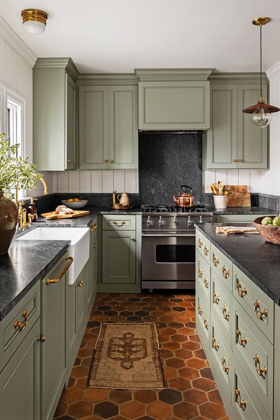 una sbalorditiva cucina vintage verde salvia con ripiani in pietra nera e alzatina, con isola cucina abbinata e maniglie e infissi dorati
