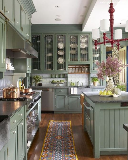 una cucina verde salvia vintage con vetri e soliti armadi, ripiani in pietra grigia, un backsplash in piastrelle bianche e un lampadario vintage