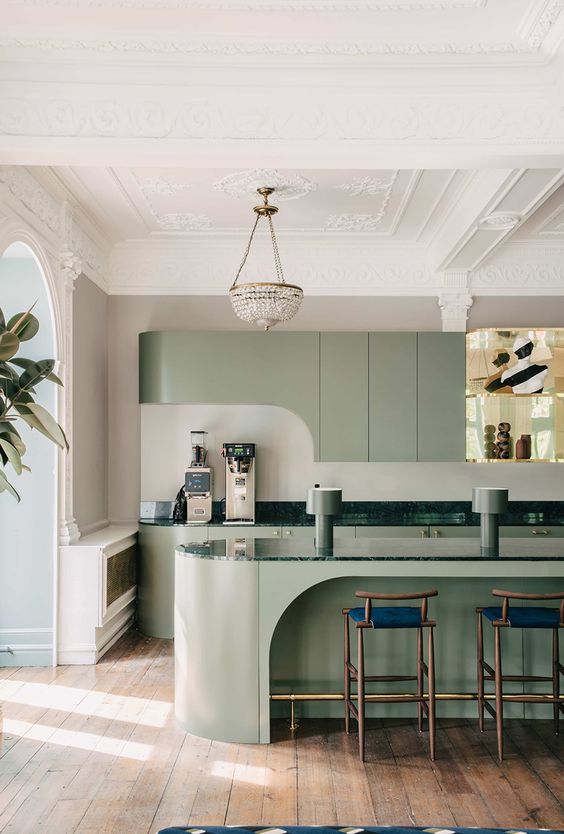 una cucina verde salvia moderna e molto raffinata con mobili curvi, un'isola scultorea della cucina e piani di lavoro verde scuro