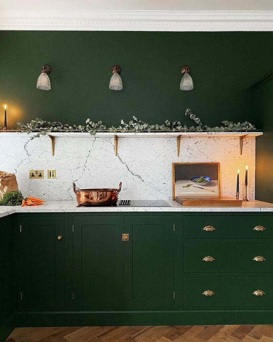 una cucina verde cacciatore con armadi vintage, maniglie dorate, un ripiano aperto con vegetazione e un alzatina in pietra bianca