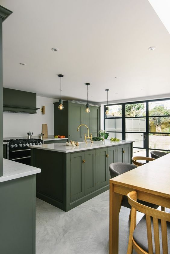 un'elegante cucina verde cacciatore con mobili vintage, alzatina e controsoffitti bianchi, lampadine a sospensione e una parete vetrata