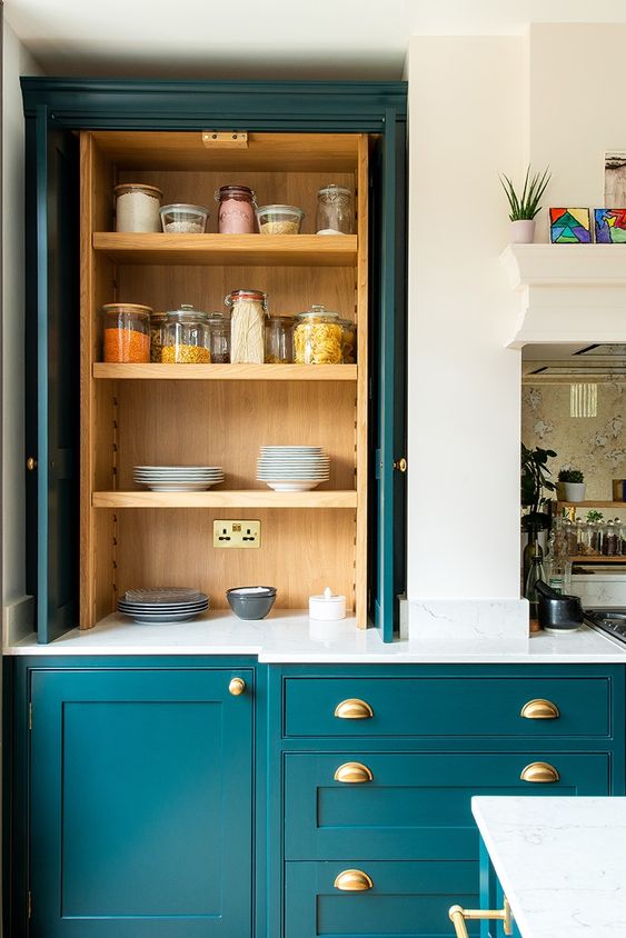 un'elegante cucina verde acqua con mobili eleganti, scomparti in legno chiaro, infissi dorati e ripiani in pietra bianca