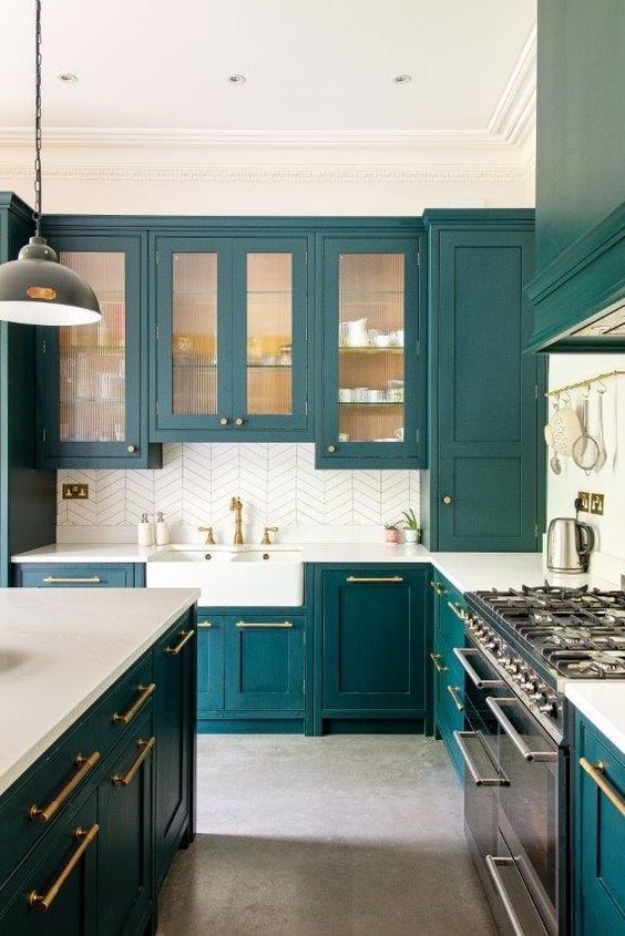 una cucina verde acqua con vetri e normali armadi, ripiani bianchi e alzatina in piastrelle bianche, finiture e maniglie dorate