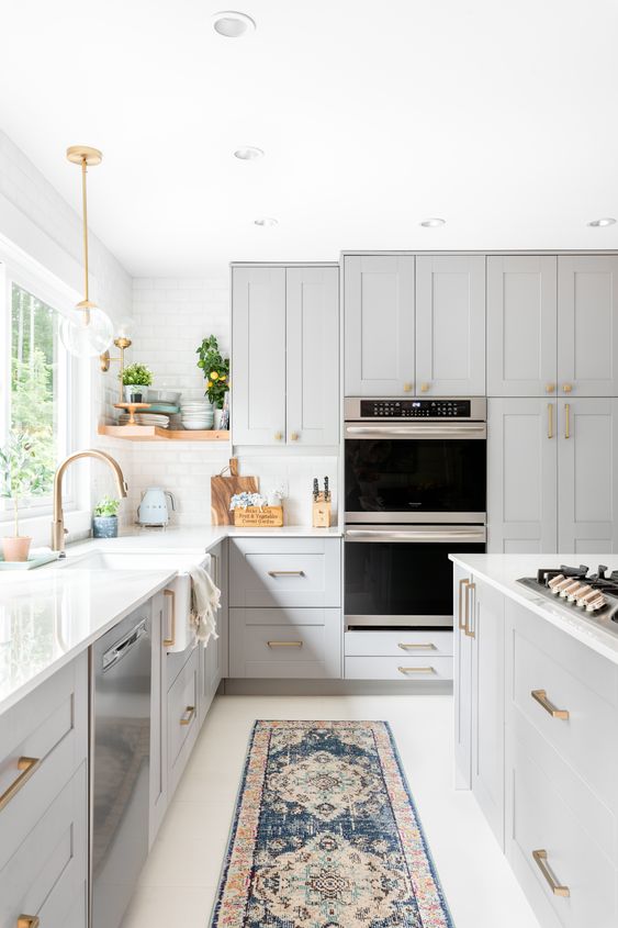una splendida cucina color tortora con ripiani in pietra bianca e alzatina in piastrelle, finiture e maniglie dorate