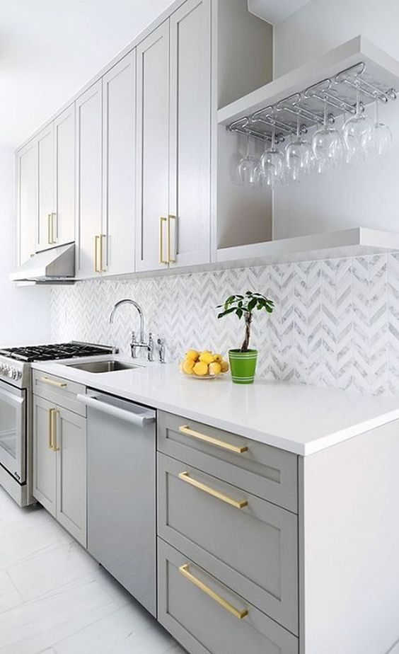 un'elegante cucina grigia con alzatina in piastrelle chevron e maniglie dorate è uno spazio elegante ed elegante