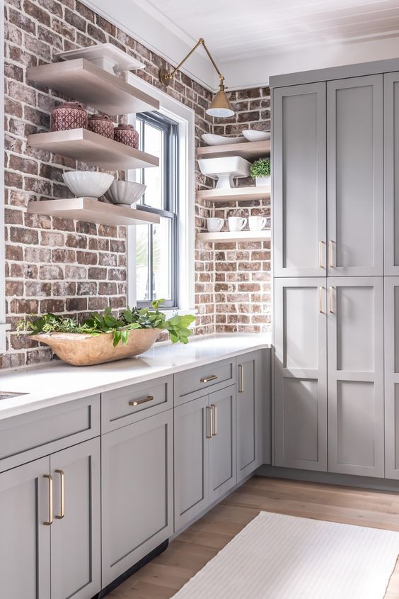 un'elegante cucina rustica grigia con armadi di ispirazione vintage, pareti in mattoni e un piano di lavoro in pietra bianca