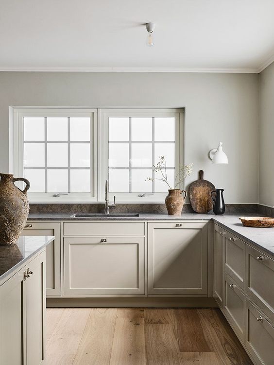 una calda e accogliente cucina scandinava grigia con mobili e pareti vintage in tinta, piani di lavoro scuri e un minuscolo alzatina