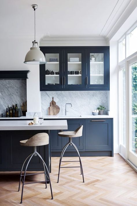 una classica cucina blu navy con armadi vintage, ripiani bianchi e alzatina in pietra bianca, lampade a sospensione vintage