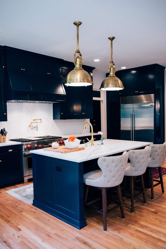 un'elegante cucina moderna blu navy con alzatina e ripiani in pietra bianca, tocchi dorati e lampade a sospensione