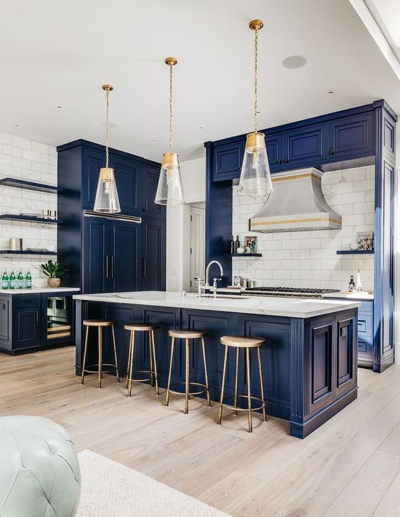 una bella cucina blu navy con armadi vintage, ripiani in marmo bianco, un backsplash in piastrelle bianche e fantastiche lampade a sospensione