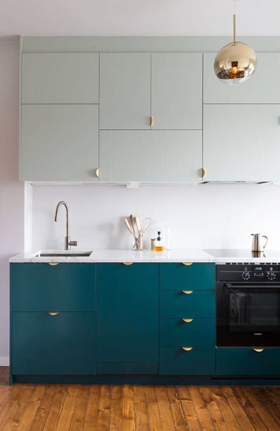 un'elegante cucina bicolore in verde chiaro e verde acqua, con maniglie dorate, una lampada a sospensione in rame e un piano di lavoro e alzatina bianchi