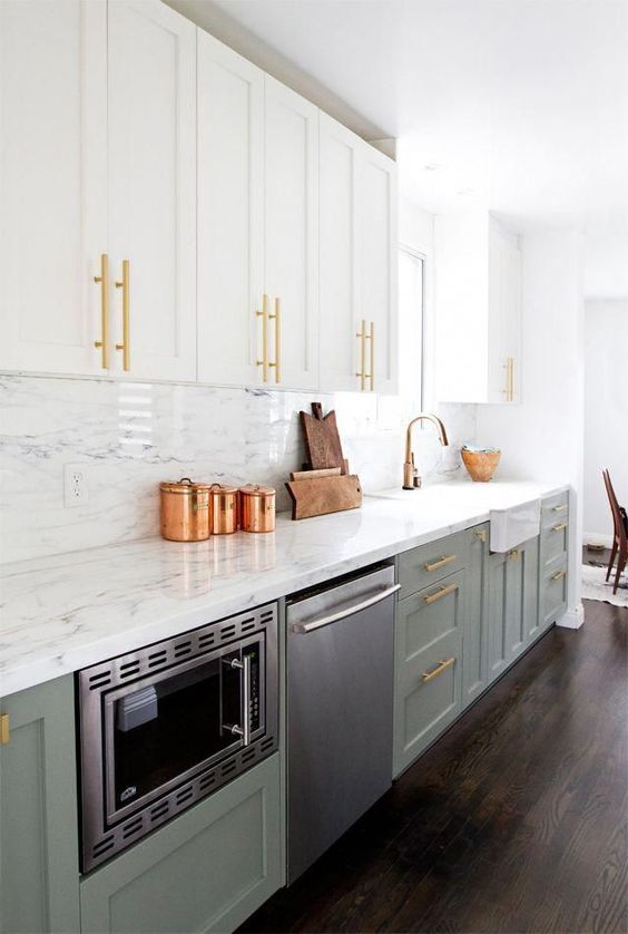 una cucina elegante e lucida con mobili bianchi e verde salvia, top e alzatina in pietra bianca, tocchi dorati