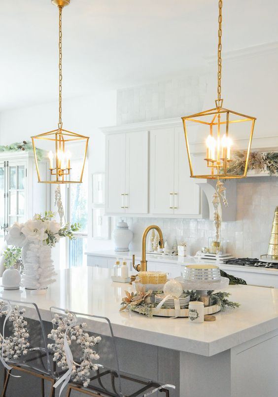una cucina neutra con un backsplash in piastrelle bianche e ripiani bianchi, lampade a sospensione dorate e infissi dorati