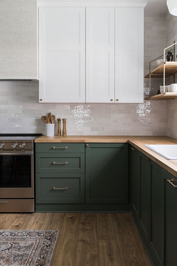 una laconica cucina verde scuro e bianca, con piastrelle in marmo bianco lucido, piano di lavoro in macellaio e infissi semplici