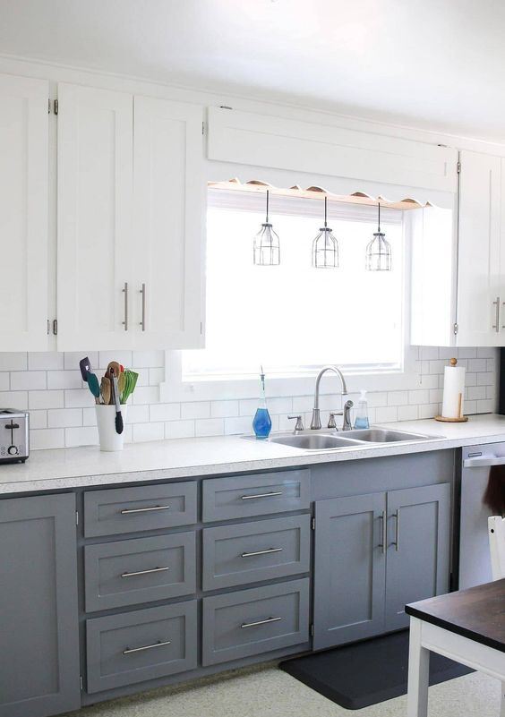 una moderna cucina colonica bicolore con ante bianche e grigie, un backsplash in piastrelle bianche della metropolitana, piani di lavoro bianchi e lampade a sospensione