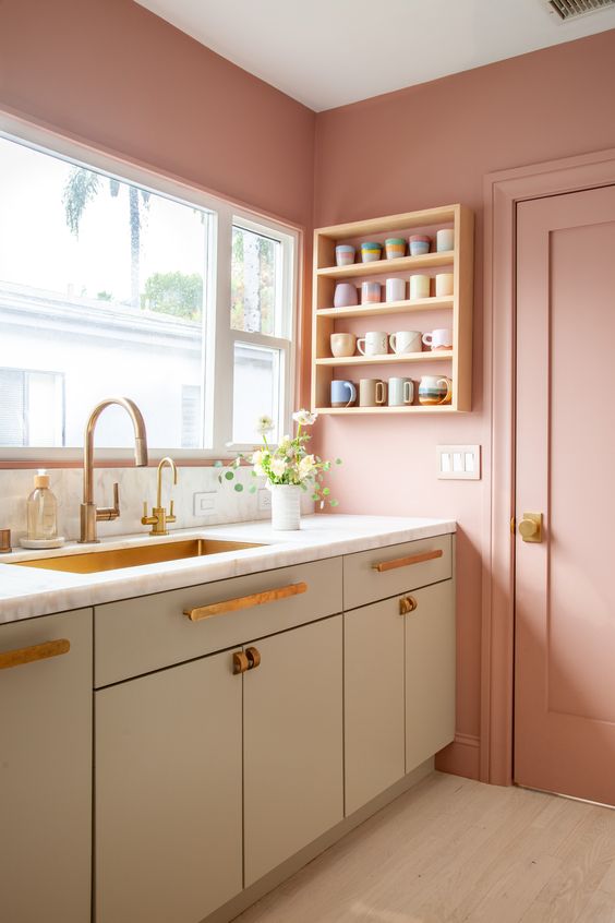 una bella cucina scandinava con pareti rosa e armadi grigi, infissi in ottone e un lavello in ottone