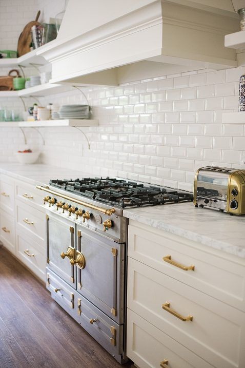 una bella cucina vintage in bianco, con un backsplash in piastrelle bianche della metropolitana e infissi dorati per un tocco più elegante