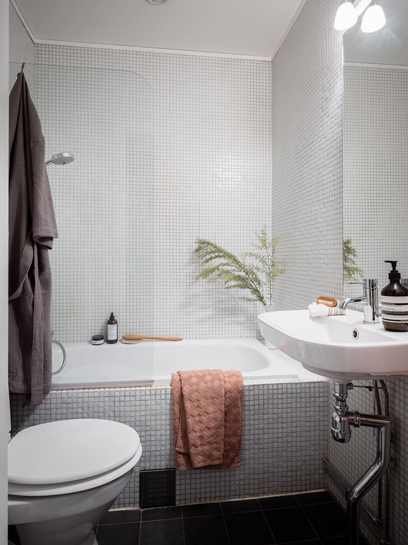 Il bagno è rivestito con piastrelle grigie su piccola scala ed elettrodomestici bianchi