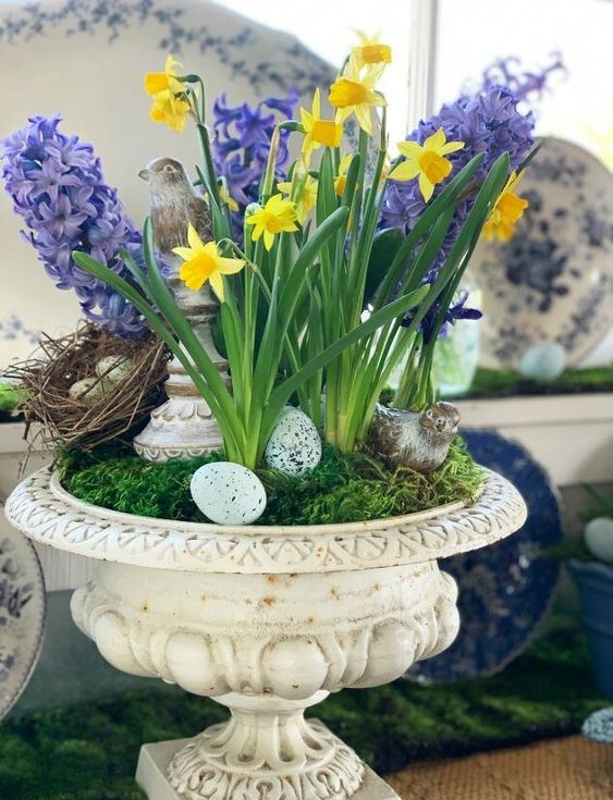 un'urna vintage con muschio, uova finte e un nido, giacinti viola e narcisi gialli per un tocco rustico e un tocco primaverile