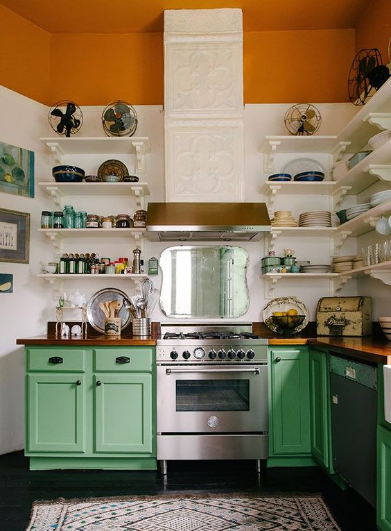 una cucina audace con pareti color block bianco e ruggine, armadi verdi, elettrodomestici in acciaio inossidabile e una cappa a motivi geometrici