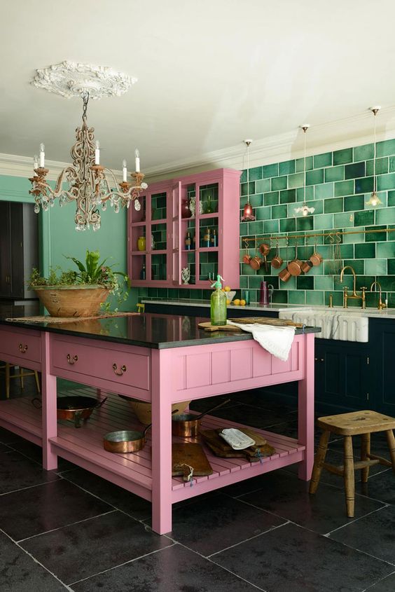 una cucina audace con mobili inferiori neri, quelli superiori rosa, un'isola della cucina rosa, un backsplash a piastrelle verdi audaci e un lampadario chic