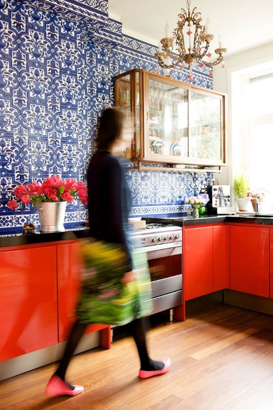 un'audace cucina rossa con una parete di piastrelle a motivi blu, un armadietto di vetro e un lampadario raffinato e chic sopra lo spazio