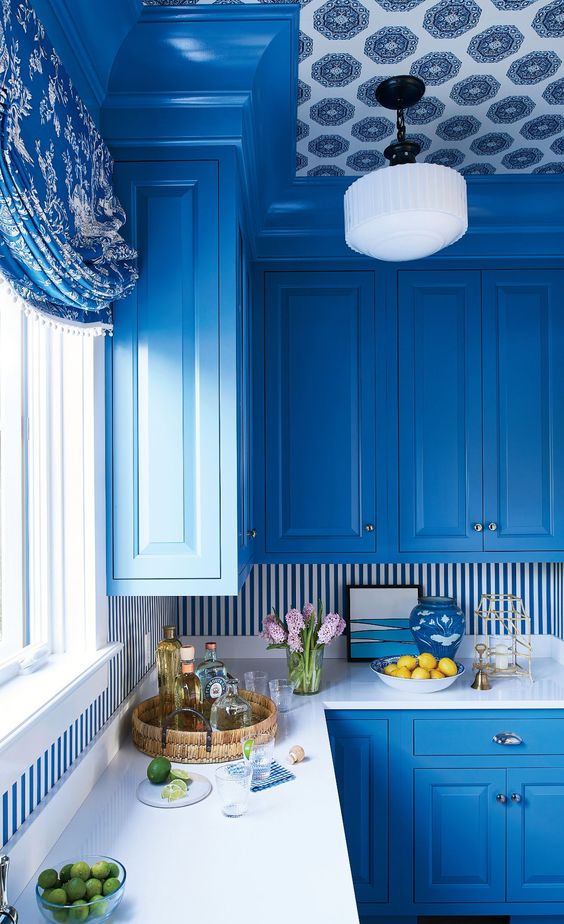 una cucina blu brillante con un backsplash a righe e un soffitto con carta da parati audace sembra molto luminosa e molto elegante, ispirata al mare