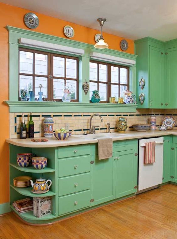 un audace cucina retrò in verde, con pareti arancioni, un backsplash in piastrelle neutre e nere e piatti decorativi sul muro