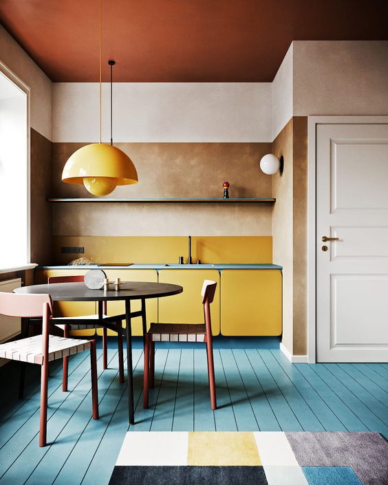 una cucina moderna e luminosa con armadi gialli e una lampada a sospensione, un pavimento blu e ripiani blu più un tappeto geometrico