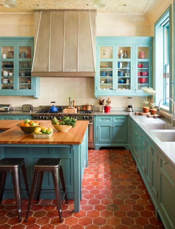 una cucina blu brillante con piastrelle in terracotta sul pavimento, una grande cappa vintage, piani di lavoro in blocco da macellaio e un soffitto a motivi geometrici