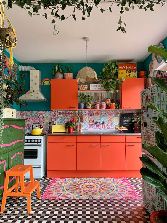 una cucina dai colori pazzi con ante arancioni, un alzatina in piastrelle colorate, un tappeto audace, pareti color smeraldo e mobili audaci