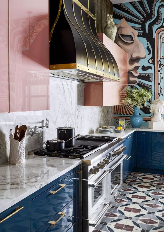 una cucina colorata con mobili inferiori blu scuro, superiori rosa, un alzatina in marmo e una cappa vintage per fare una dichiarazione