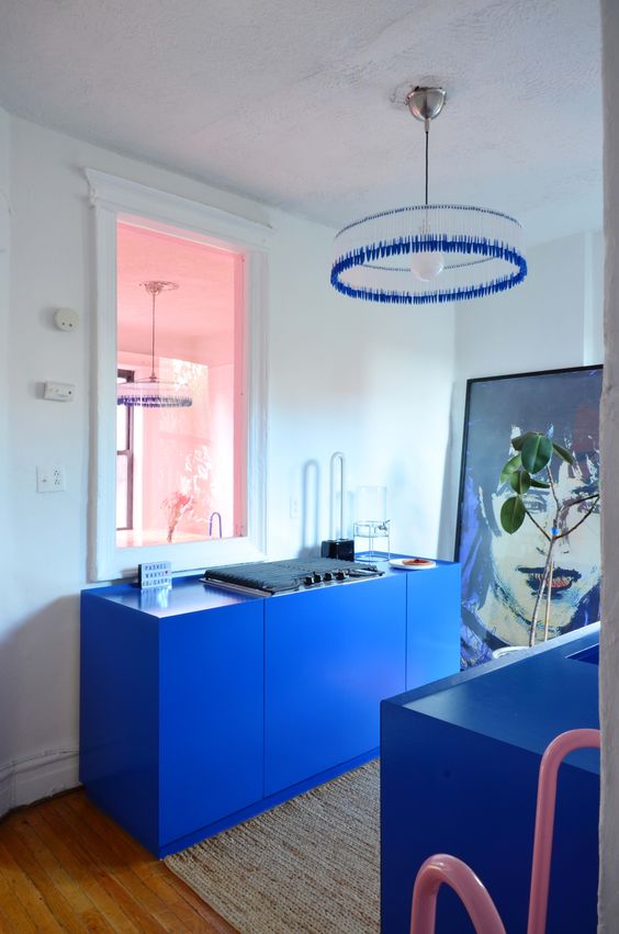 una cucina blu super audace, ma piccola con non molti armadi, un'opera d'arte e un lampadario blu brillante
