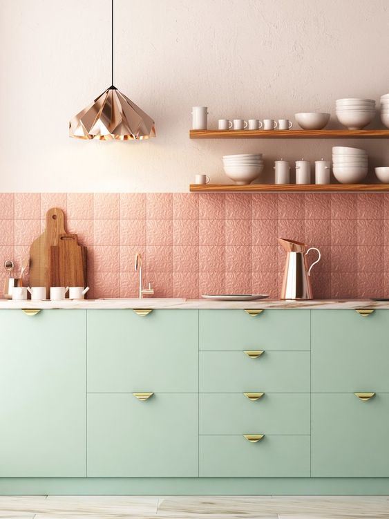 una bella cucina contemporanea con mobili color menta e maniglie dorate, piastrelle rosa fantasia e strutturate, una lampada a sospensione geometrica in rame