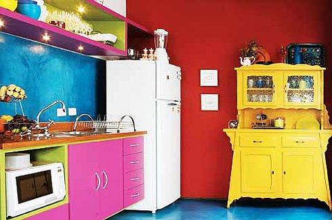 una cucina pazza e colorata con un audace muro blu e rosso acceso, un buffet giallo brillante, armadi rosa caldo e nicchie in verde, con luci