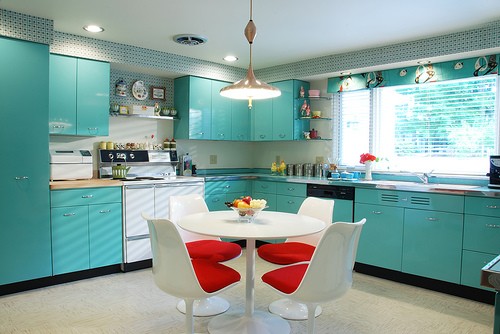 una cucina colorata con mobili vintage bianchi, piastrelle blu e verdi, una bella carta da parati floreale, tende a quadri verdi è uno spazio divertente e alla moda