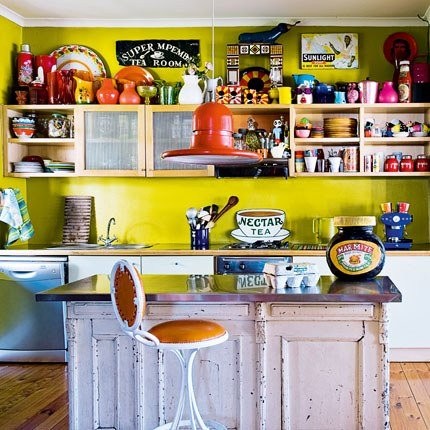 una cucina divertente e colorata con pareti color senape, contenitori aperti e chiusi, un'isola cucina shabby chic e sgabelli, oltre a tanti decori e accessori